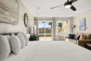 A bedroom with a large bed, a ceiling fan, a view of a pool, and a balcony with a railing. - The Ambassador - Unit C5 - Studio King - On Pool Deck (Panama City Beach)