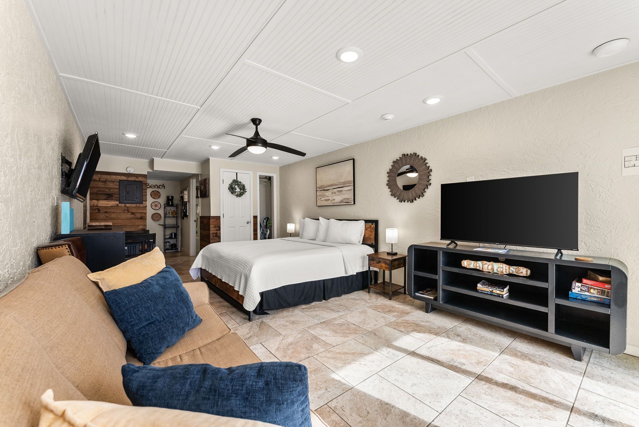Een slaapkamer met een bed, een televisie, een plafondventilator en een tv-meubel met planken.