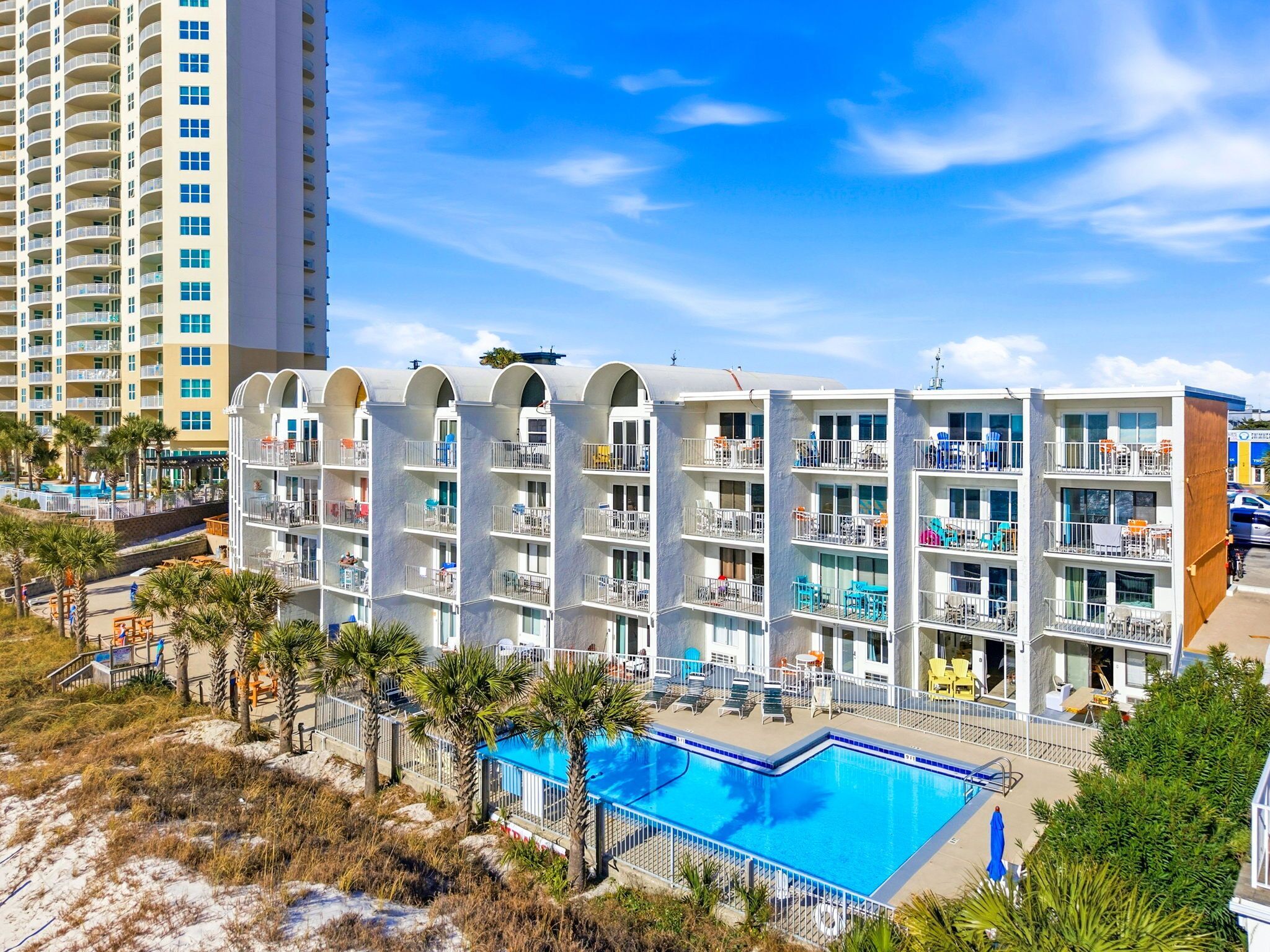 Ein mehrstöckiges Hotel mit Balkonen, einem Schwimmbad und Blick auf den Strand.