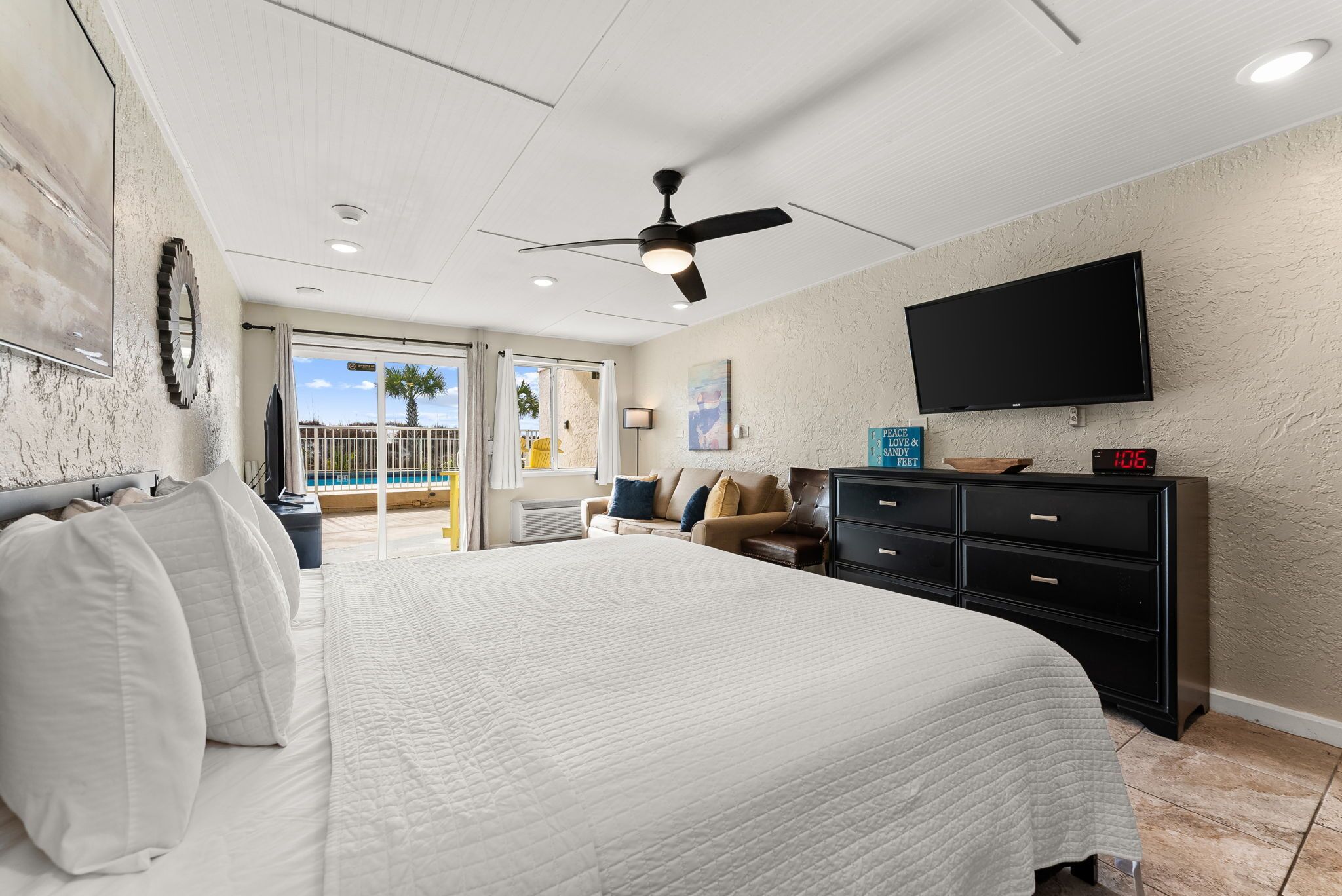 A bedroom with a bed, a ceiling fan, a TV, a nightstand, a dresser, and a view of the outdoors.