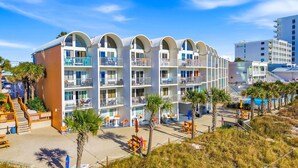 A beachfront hotel with multiple balconies, outdoor seating, and a sandy beach area. - The Ambassador - Unit C5 - Studio King - On Pool Deck (Panama City Beach)