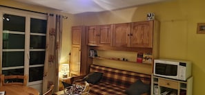 A compact living space with a dining table, a sofa, wooden cabinets, a microwave, and a window with curtains. - Apartment “Les Granges 13” with Mountain View, Balcony and Wi-Fi (Villard-Reculas)