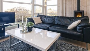 Un salon avec un canapé en cuir noir, une table basse blanche, un téléviseur et un poêle à bois.