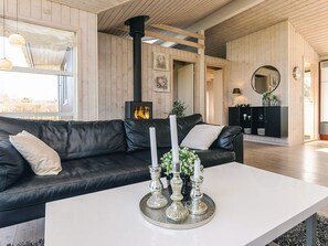 A modern living room with a black leather sofa, a white coffee table with silver candle holders, a wood-burning stove, and a black cabinet with decorative items. - 4 Star Holiday Home in Svendborg (Svendborg)