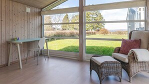 Une pièce avec un plafond en bois, une grande fenêtre, une table avec une chaise et des meubles en osier.