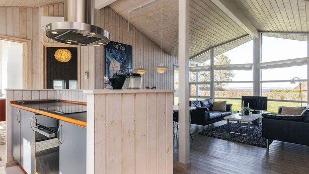 Une cuisine moderne avec un îlot central en bois, un coin repas avec un canapé en cuir noir et une grande fenêtre offrant une vue dégagée.