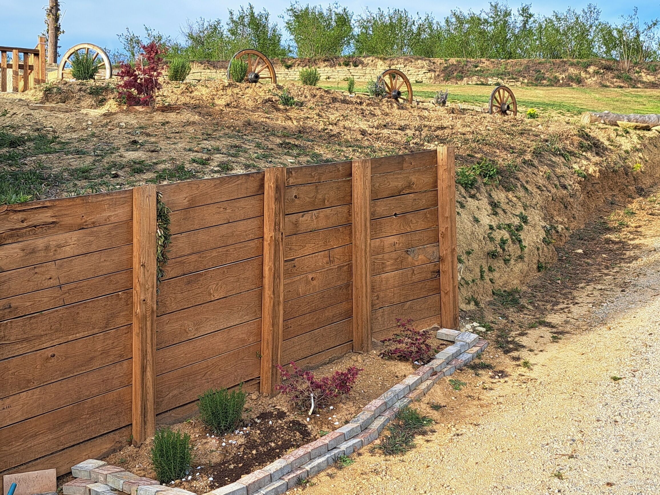 A wooden fence with a brick pathway and small plants.