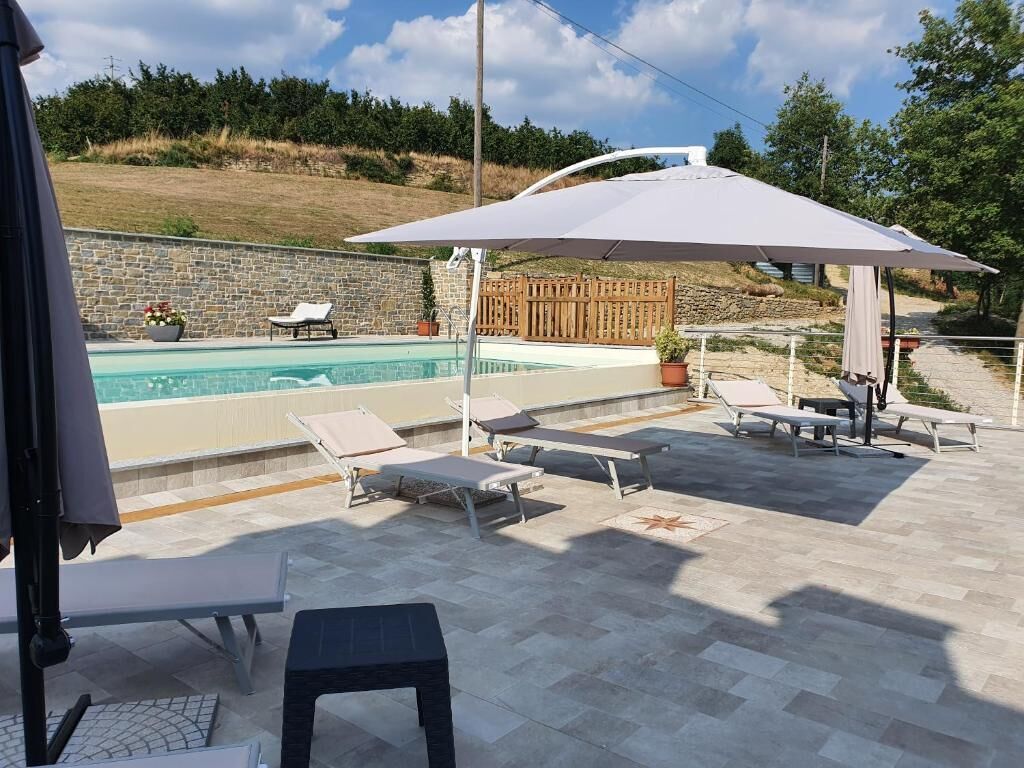 Ein Außenpoolbereich mit Liegestühlen und Sonnenschirmen, eine Steinmauer und ein Blick auf die umliegende Landschaft.