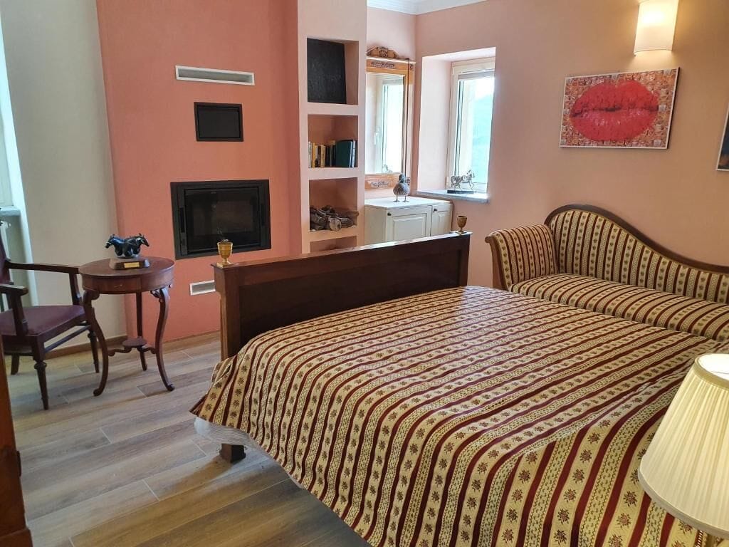 Un dormitorio con cama, una silla, televisor, estante con libros y ventana con vistas.