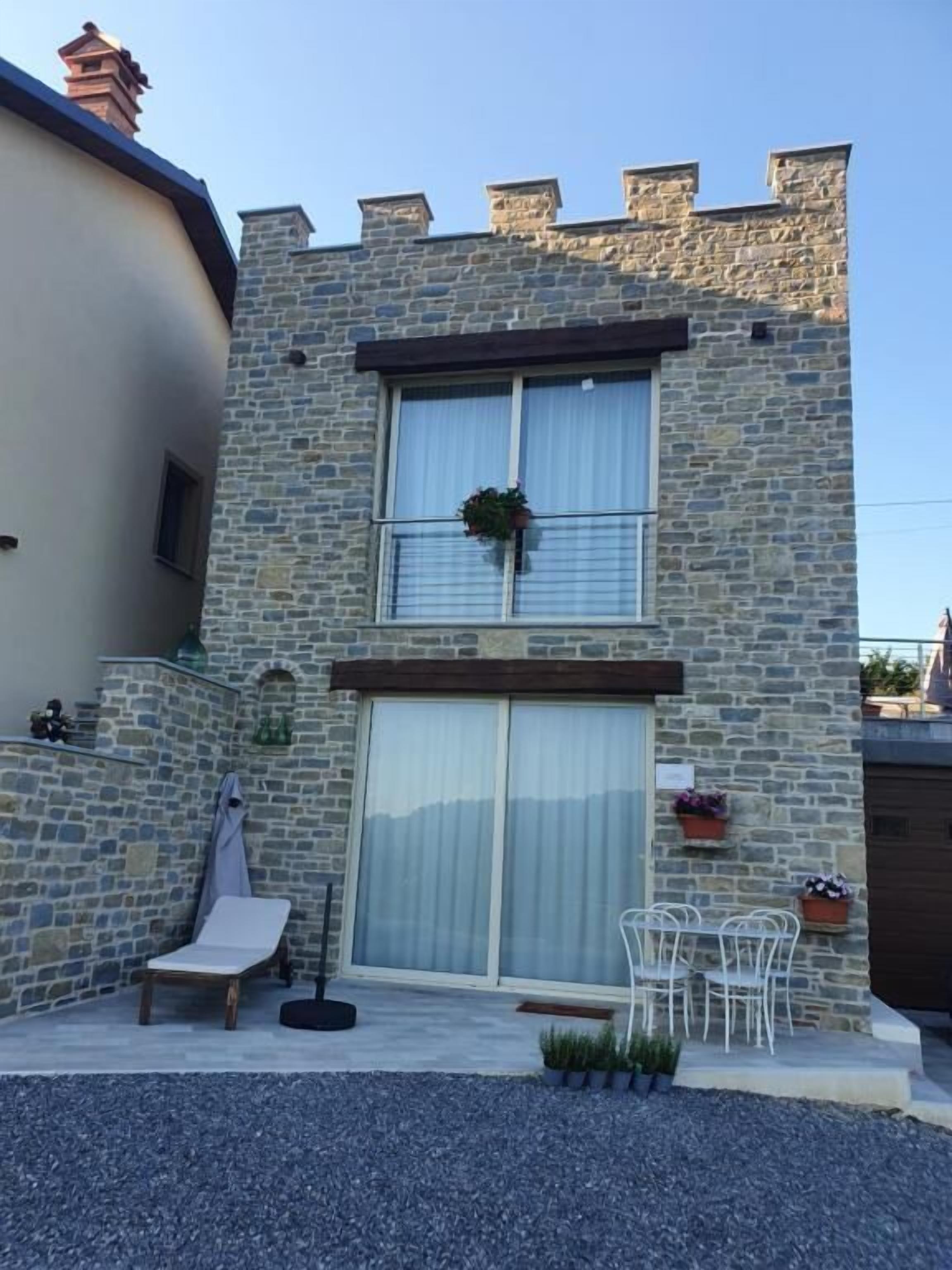 Un bâtiment en pierre de deux étages, doté d’un balcon, d’une porte-fenêtre coulissante et d’un espace extérieur aménagé pour s’asseoir.