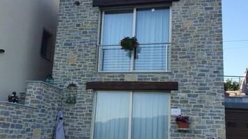 Un bâtiment en pierre de deux étages, doté d’un balcon, d’une porte-fenêtre coulissante et d’un espace extérieur aménagé pour s’asseoir.