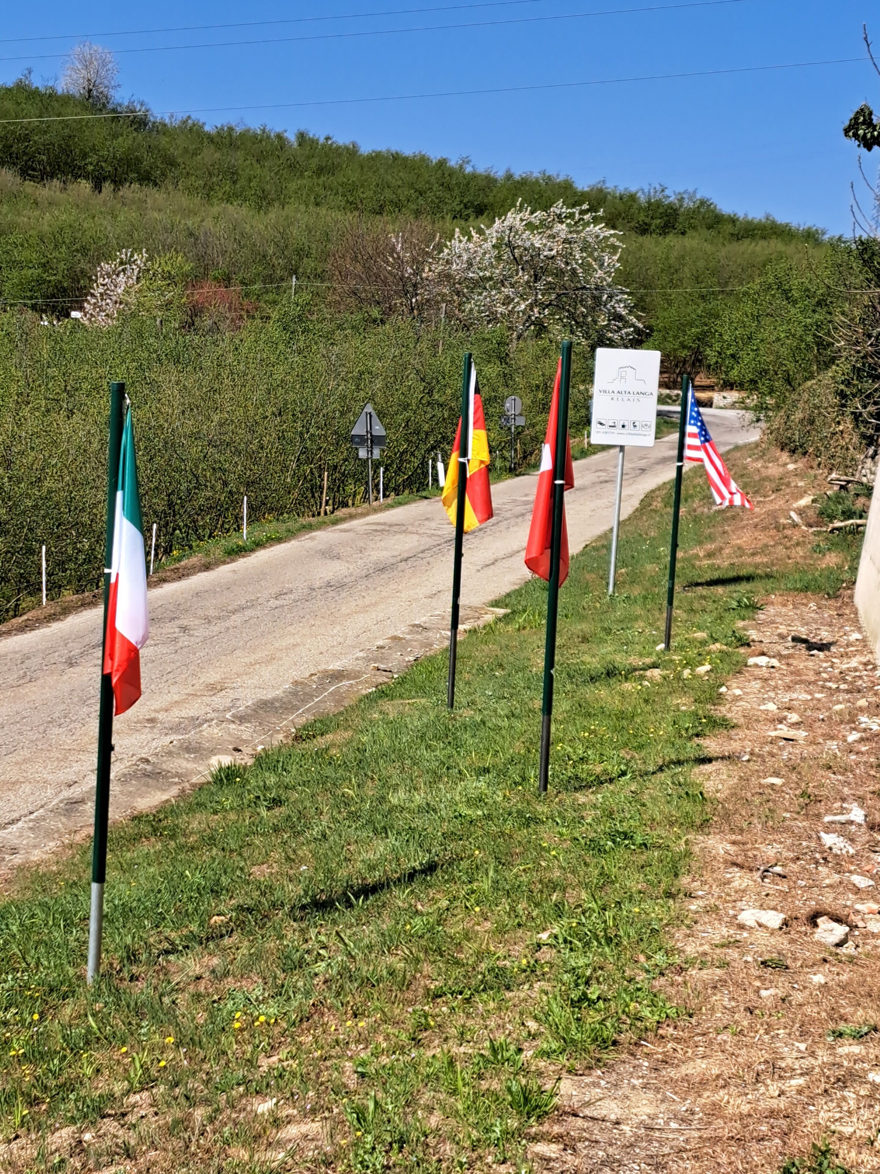 Una carretera con varias banderas y un cartel que indica Villa Alta Langa.