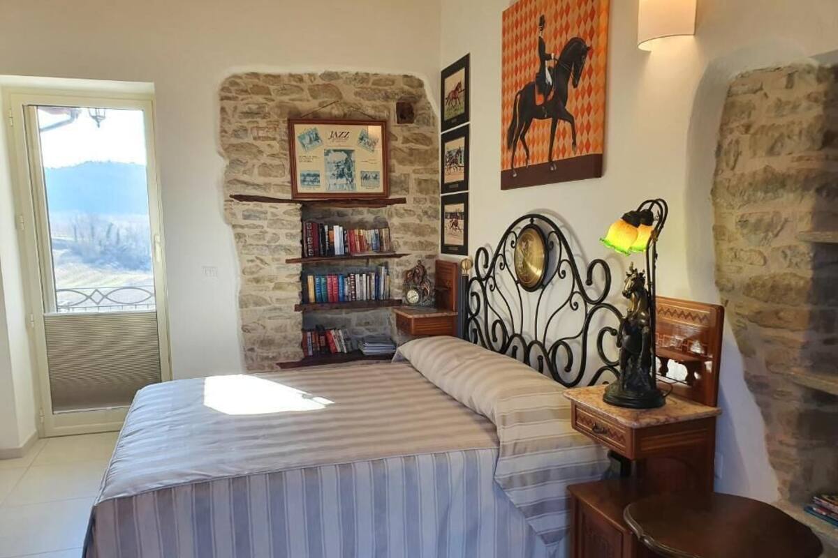 Ein Schlafzimmer mit Bett, Bücherregal, aufgehängtem Bild, Lampe und einer Steinwand.