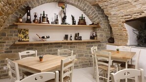Un coin repas rustique avec des murs en pierre, des tables en bois et des chaises blanches.
