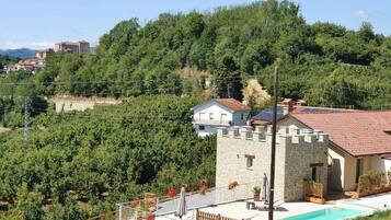 Une maison en pierre avec une piscine, entourée d’une végétation luxuriante et de collines.