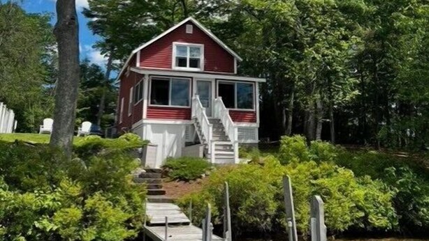 A red cabin with a staircase leading to a dock over water, surrounded by dense greenery. - Sunset Bungalow on Lake Winnisquam (Belmont)