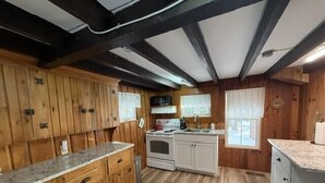 A wooden cabin-style kitchen with a central island, white cabinets, and a large window. - Sunset Bungalow on Lake Winnisquam (Belmont)