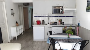 Eine moderne Küche mit weißen Schränken, einer Mikrowelle und einer Kaffeemaschine. Ein Esstisch mit Stühlen und ein kleiner Topfpflanze sind ebenfalls vorhanden.