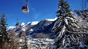 Ein verschneites Bergstädtchen mit Bäumen, einer Seilbahn und blauem Himmel.