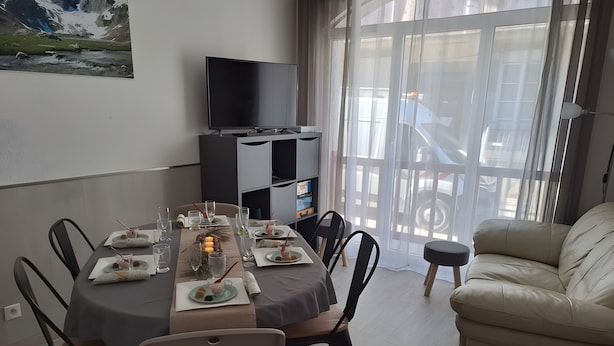 Ein Essbereich mit einem für sechs Personen gedeckten Tisch, Stühlen, einer Couch, einem Fernseher und einem fenster mit Vorhängen.