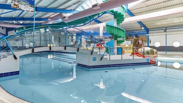 Een binnenzwembad met een grote glijbaan, een bord met daarop 'Welcome to Splashland', en een overdekt gebied met zitplaatsen.