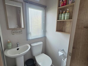 A bathroom with a sink, toilet, and window blinds. - Pines 15 (Porthcawl)