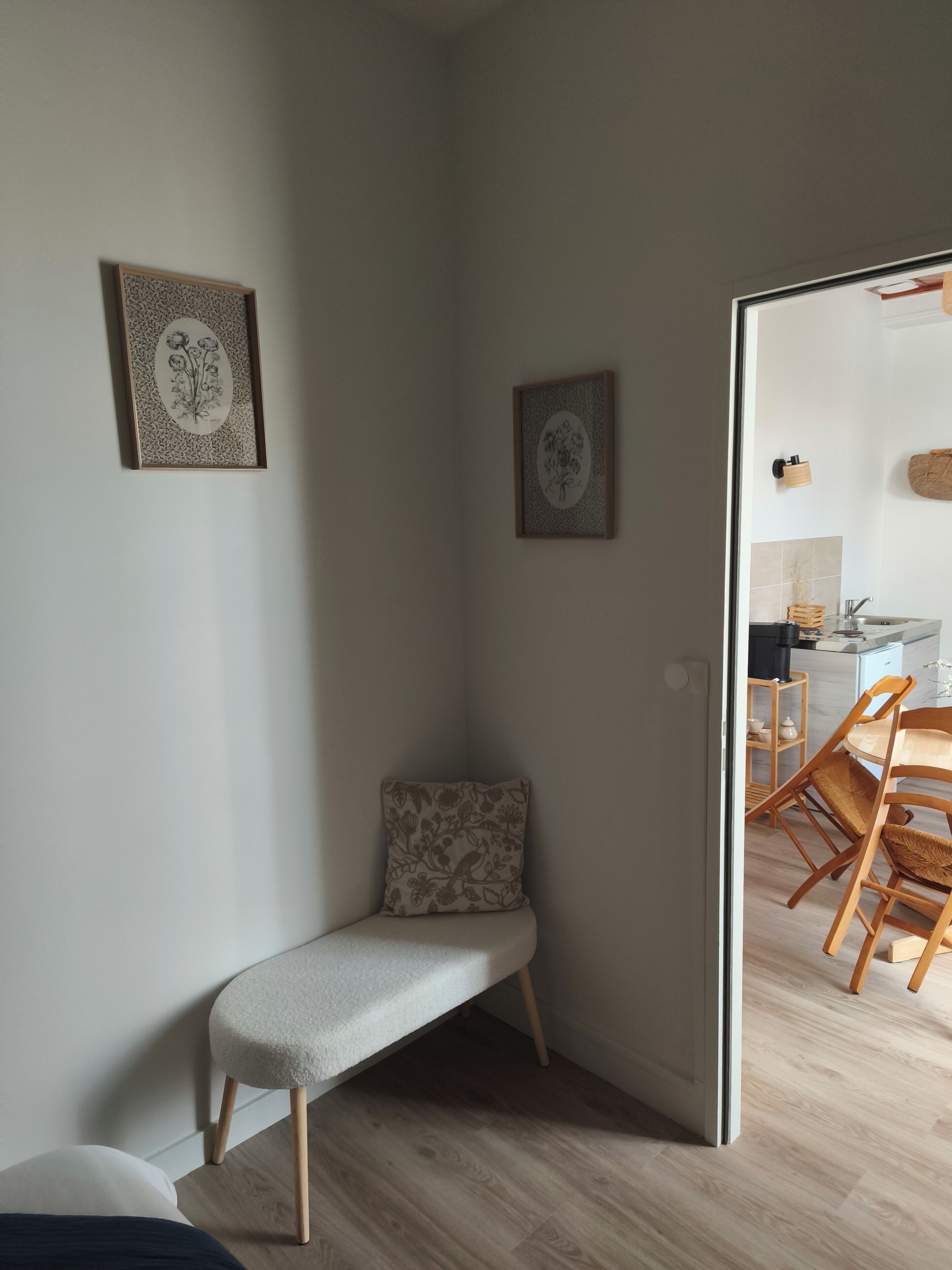 Un rincón de habitación con un banco, un cojín y dos obras de arte floral enmarcadas en la pared.