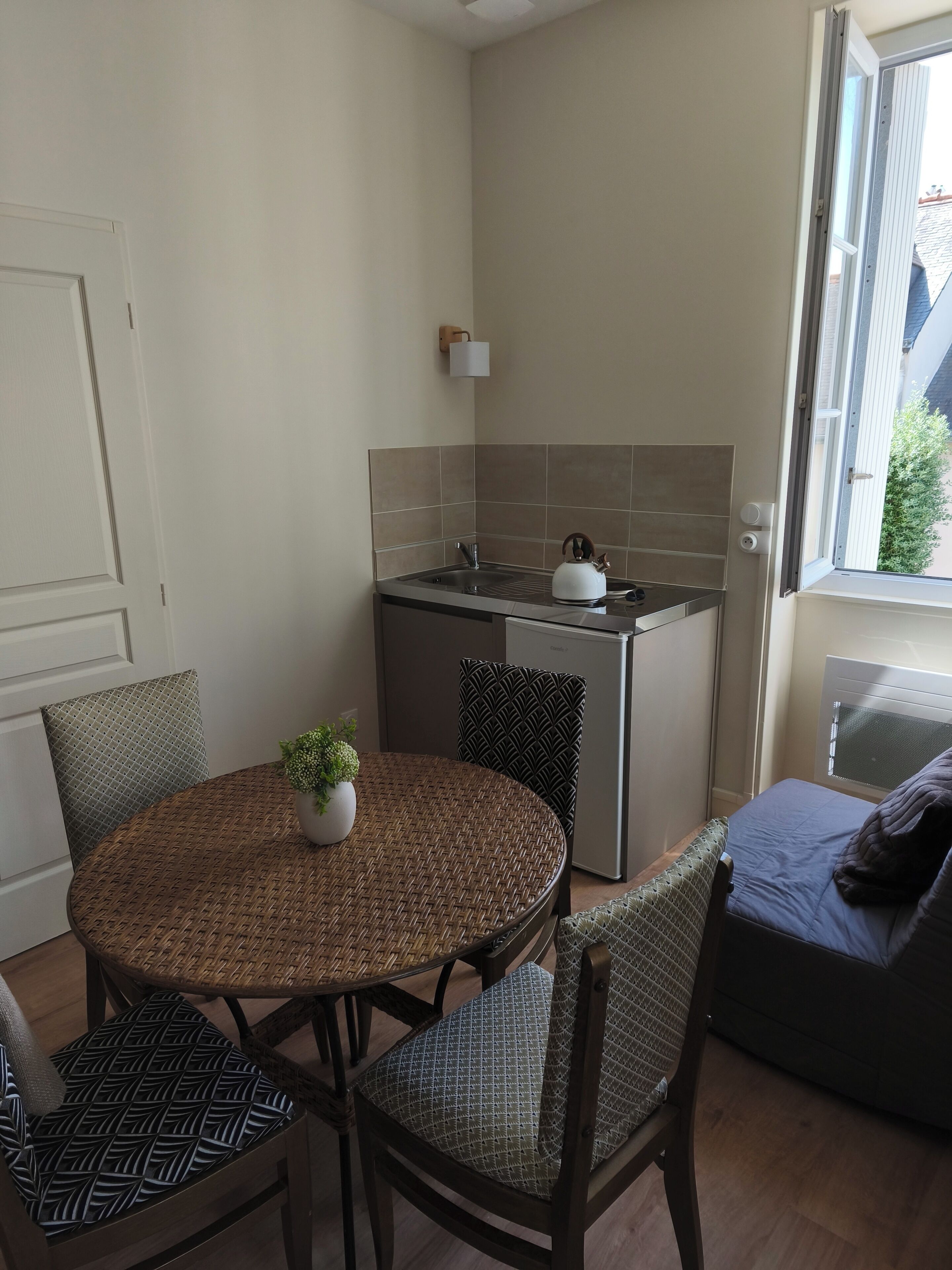Cocina compacta con lavamanos, hervidor y un pequeño comedor con una mesa redonda y dos sillas.