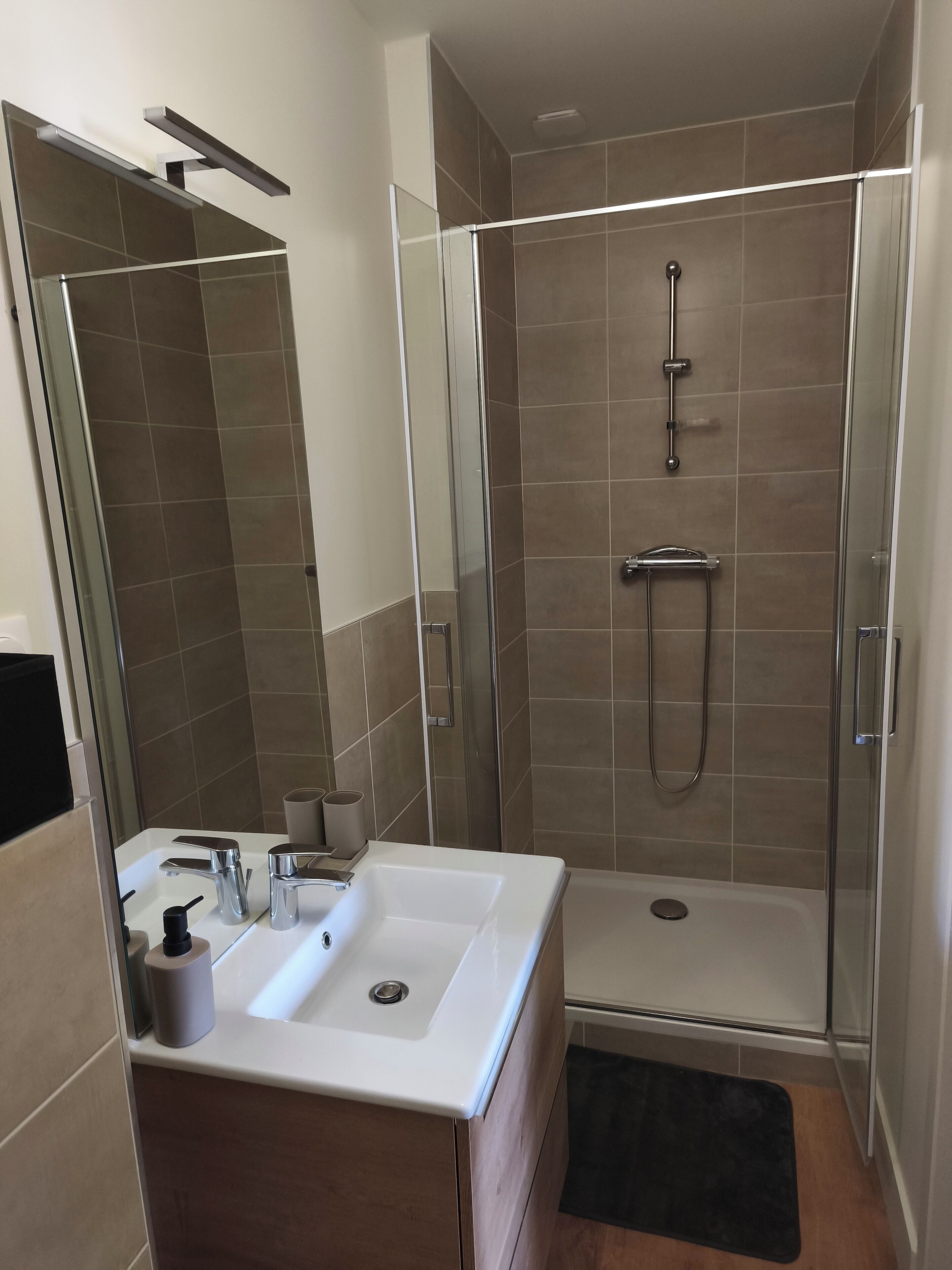 Un baño moderno con ducha de vidrio, lavamanos blanco y espejo.