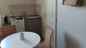 A compact kitchen with a coffee machine, a sink, and a small refrigerator. There is a dining area with a round table and wicker chairs.