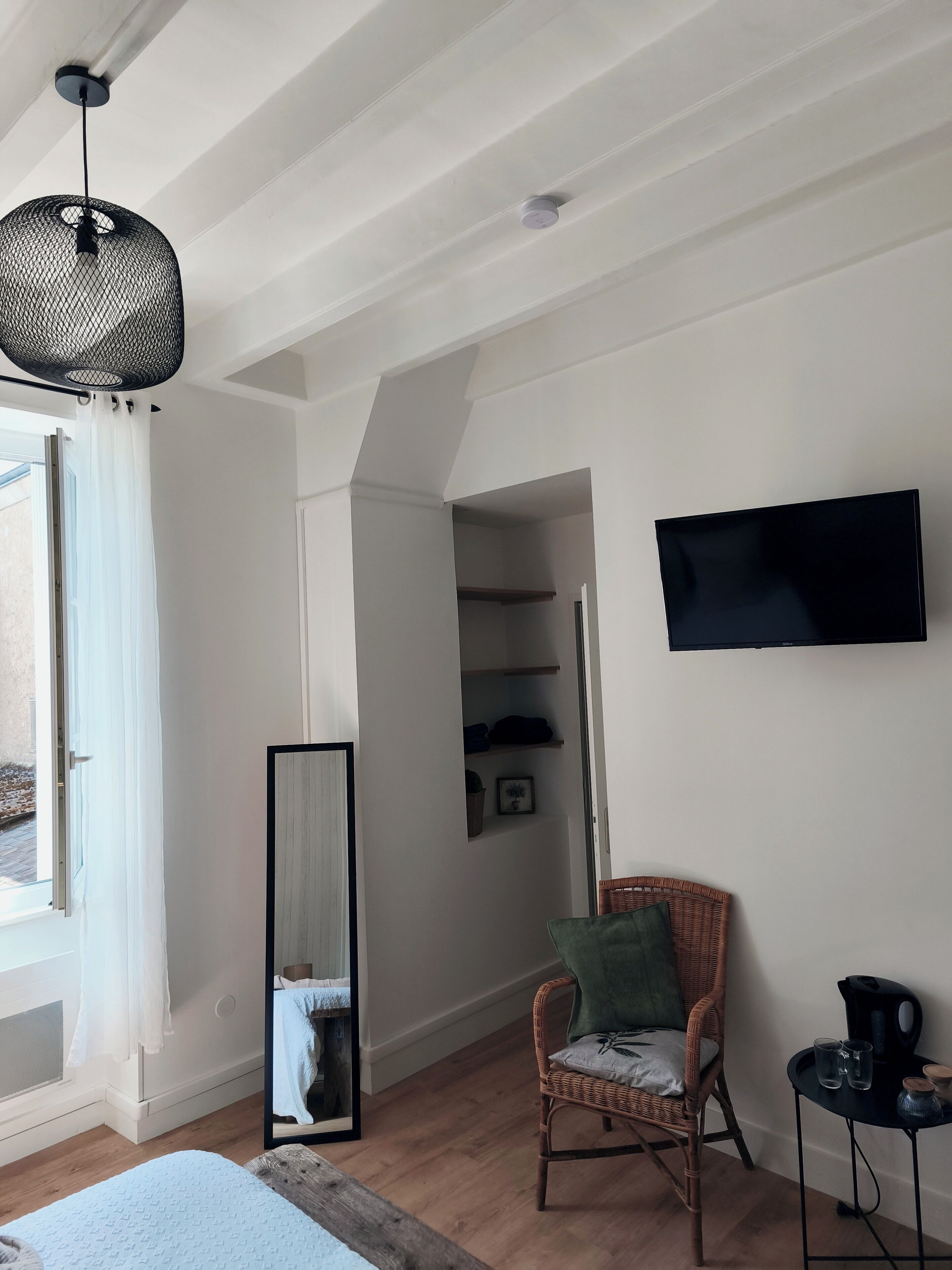 A room with a bed, a chair, a TV, and a large mirror.