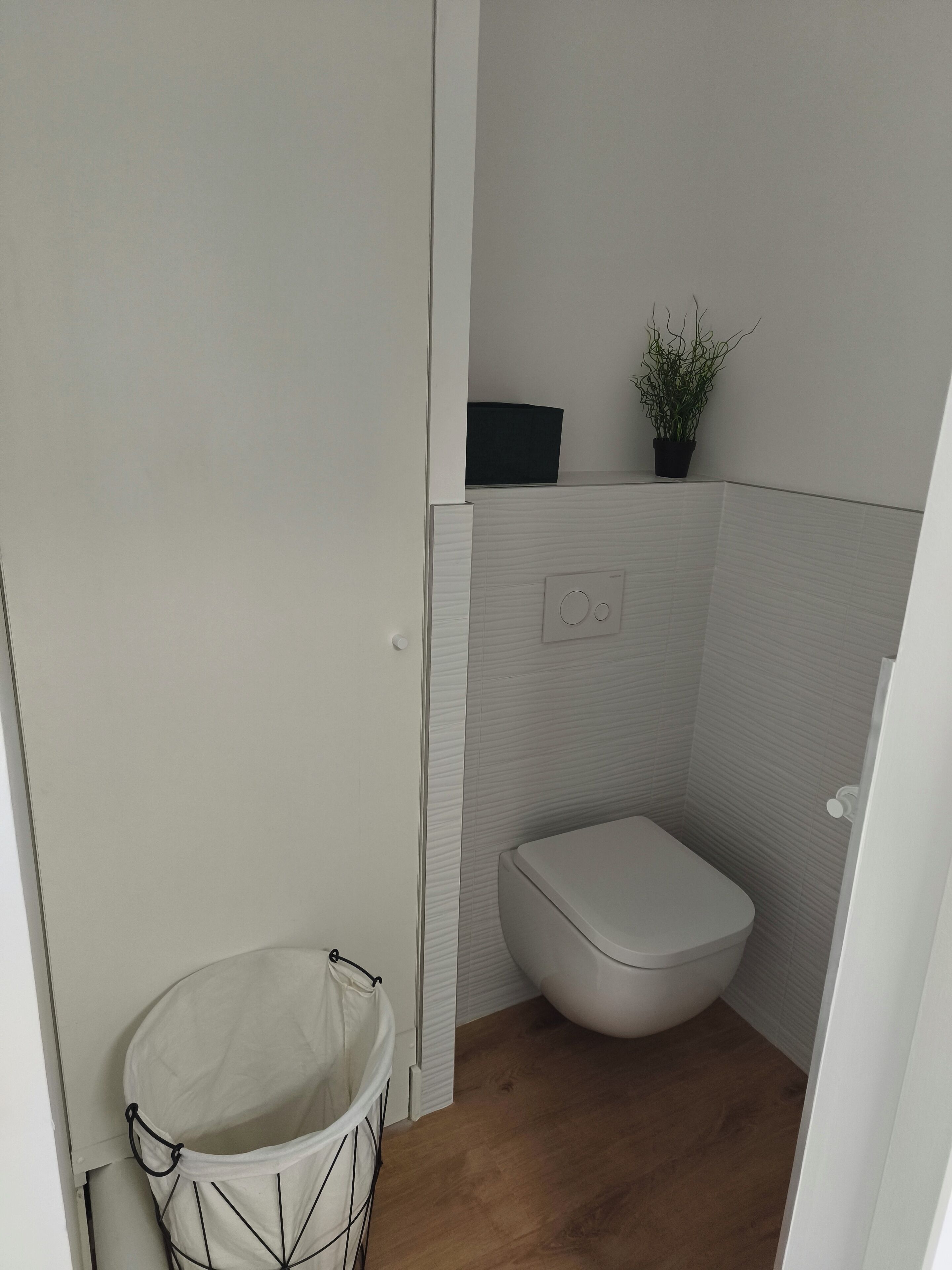 Une petite salle de bain compacte, équipée de toilettes, d’une poubelle et d’une plante en pot accrochée au mur.