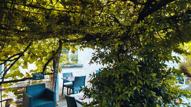 An outdoor seating area with wicker furniture and a table, surrounded by lush green foliage.