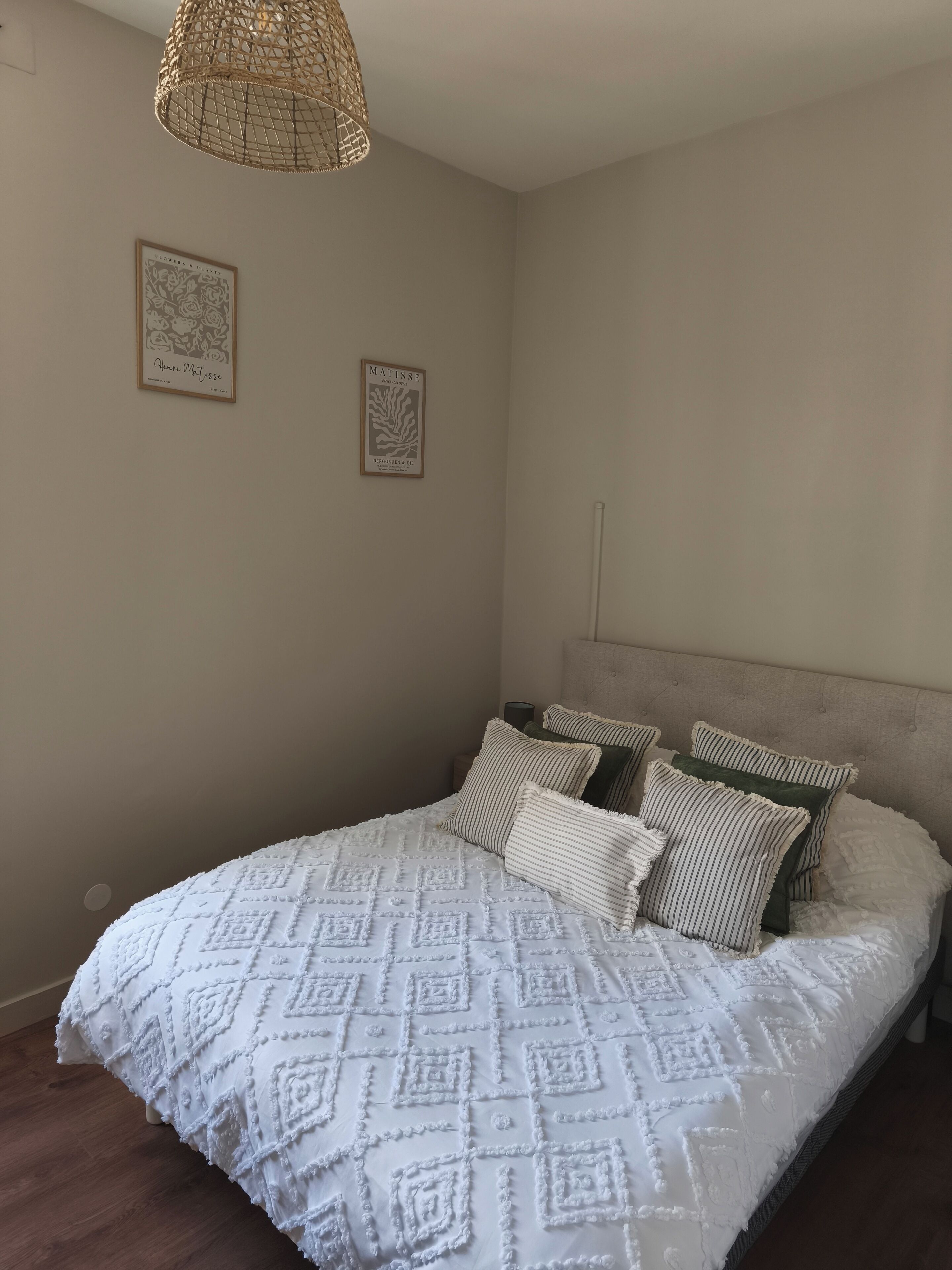 A bedroom with a large bed, a woven light fixture, and two framed artworks on the wall.