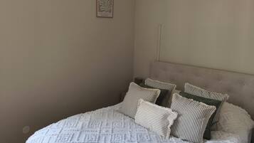 A bedroom with a large bed, a woven light fixture, and two framed artworks on the wall.