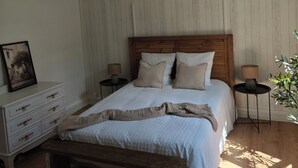 A bedroom with a wooden bed, a bench, a nightstand, a lamp, and a framed picture on a dresser.