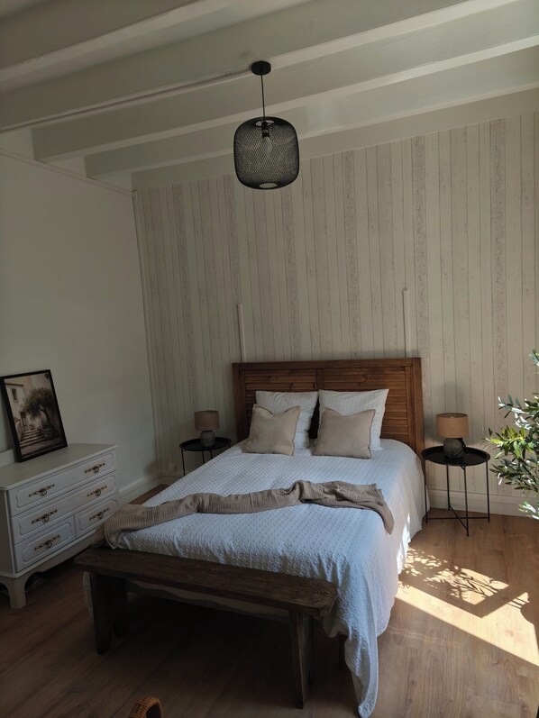 A bedroom with a wooden bed, a bench, a nightstand, a lamp, and a framed picture on a dresser.