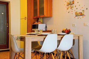 A dining area with a wooden table, white chairs, and a microwave on the counter. - Bright Flat Over the Hills of Lake Garda (Villanuova sul Clisi)