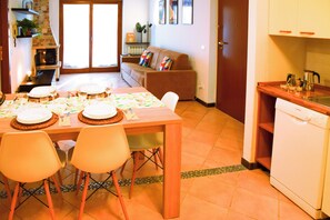 A dining area with a wooden table set for four, a sofa, and a kitchen area with a dishwasher. - Bright Flat Over the Hills of Lake Garda (Villanuova sul Clisi)