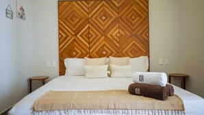 A hotel room with a large bed, a wooden headboard, multiple pillows, a blanket, and two bedside tables. - Work & Relax apto fast wifi (Tulum)