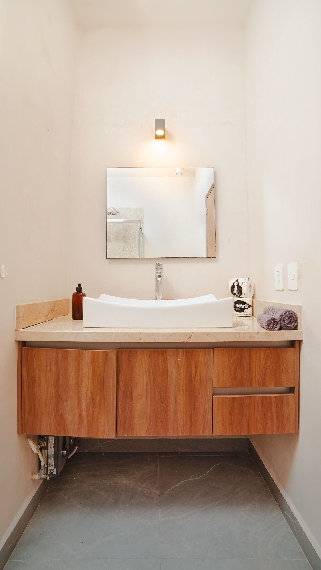 A bathroom with a wooden vanity, a white sink, a mirror, a soap dispenser, and a towel.