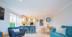 A modern living room with two sofas, a kitchen in the background, and a dining area with a table and chairs.