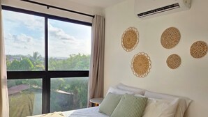 Habitación de hotel con un ventanal grande, una cama con ropa blanca y adornos tejidos en la pared.