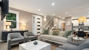 En moderne stue med sofa, to lænestole, et sofabord og et spiseområde med bord og stole.