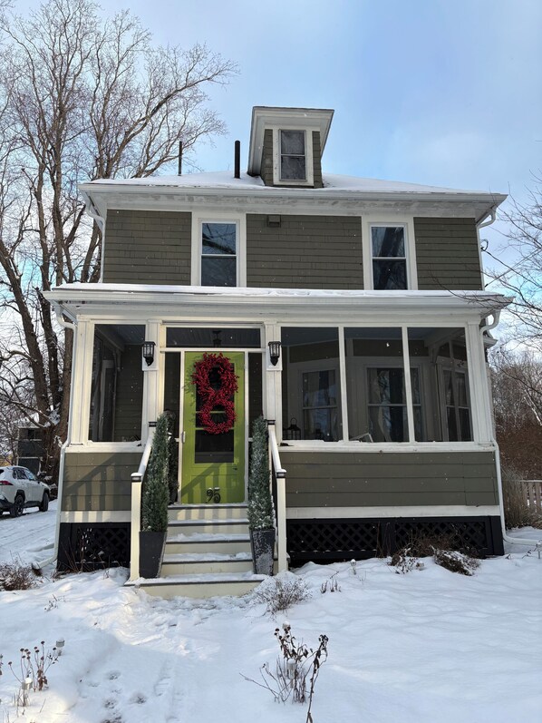 A two-story house with a green door, a red wreath, and a small porch.