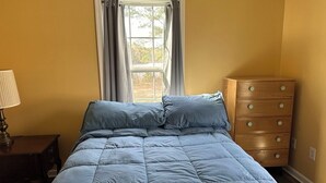 A bedroom with a bed, a dresser, a lamp, and a window with curtains.