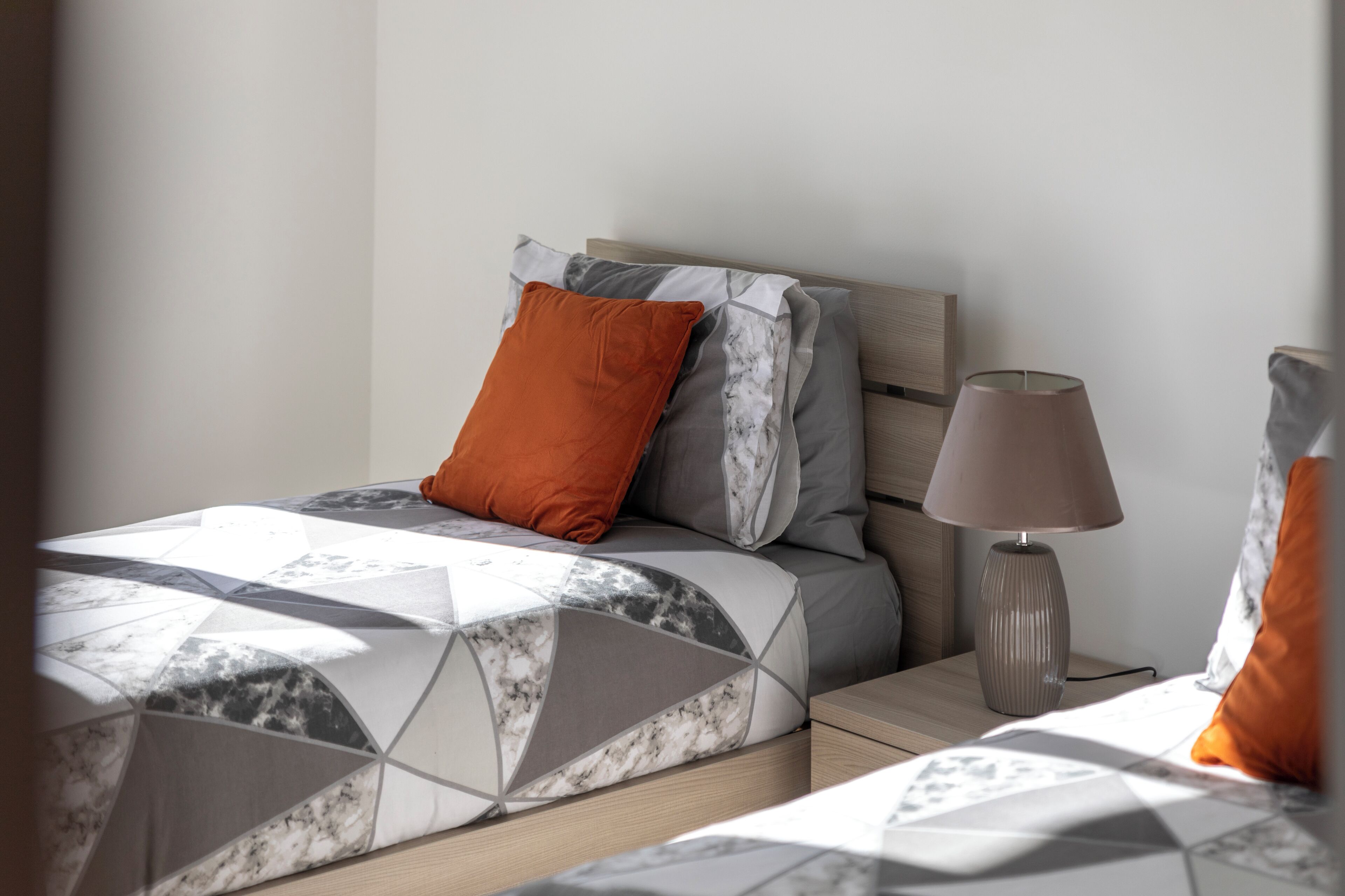 Una cama bien hecha con una colcha de estampado geométrico, un cabecero de madera y una lámpara de noche.