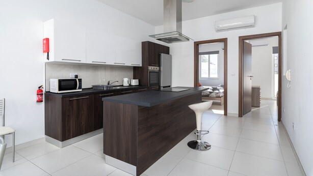 Una cucina moderna con mobili in legno scuro, un frigorifero in acciaio inossidabile, un forno a microonde e una grande isola con uno sgabello da bar.