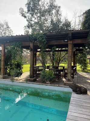 A wooden pergola with benches, a pool, and surrounding greenery. - Le Marais de Capeau, private with pond, swimming pool and leisure facilities (Arles)