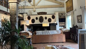 Ein geräumiges Wohnzimmer mit hoher Decke, Holzbalken, einem Kamin, einem großen Sofa, einem Esstisch und einem Cowhide-Teppich.